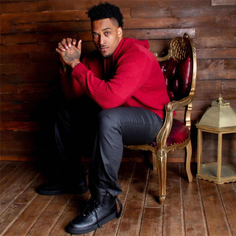 Joe Barksdale personal branding photo sitting in red velvet chair with gold trim wearing red shirt black pants  black shoes elbows on knees hands clasped together near face