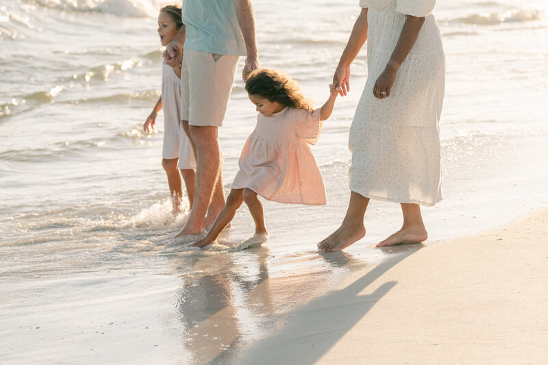 young family holding hands walking into the water