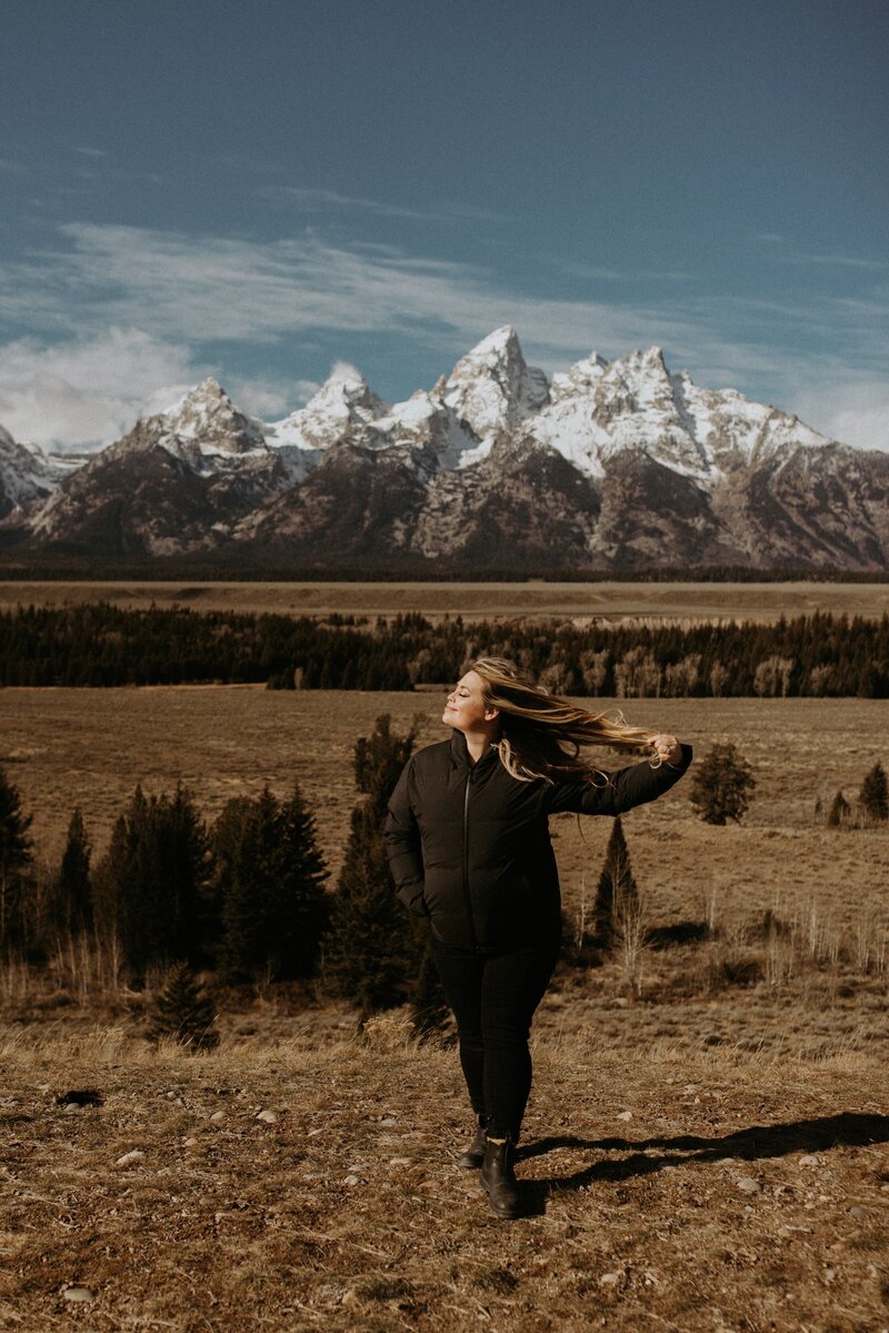 woman standing in front of mountains and holding her hair