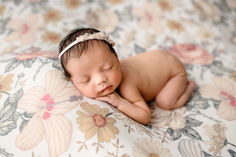 newborn baby girl wears a headband and is posed on her belly on a flower studio background