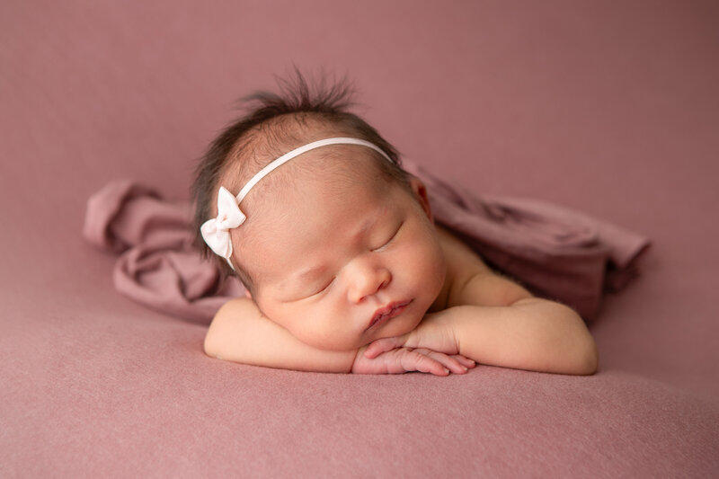 Chin on hands studio table pose newborn baby girl