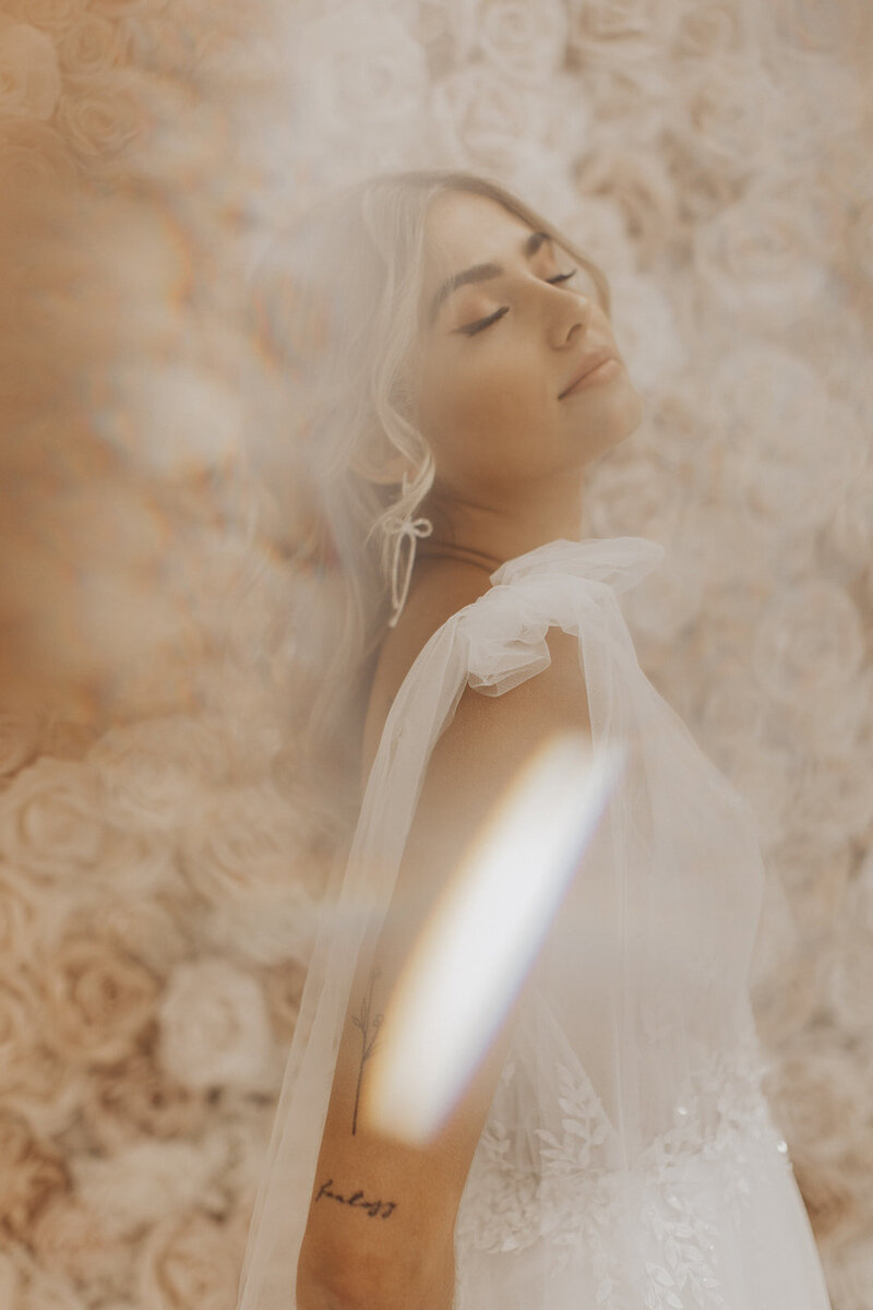 A bride in a delicate white gown with her eyes closed, featuring a lens flare.