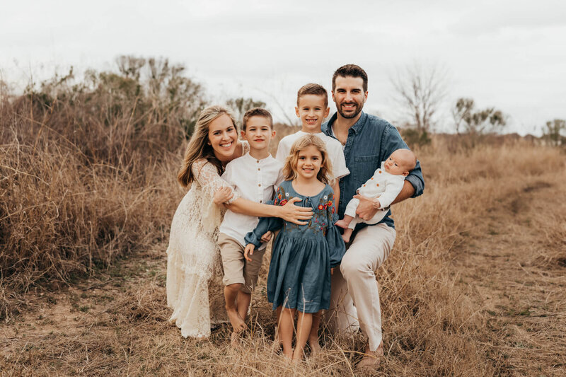 family loves on baby brother in a field family session.