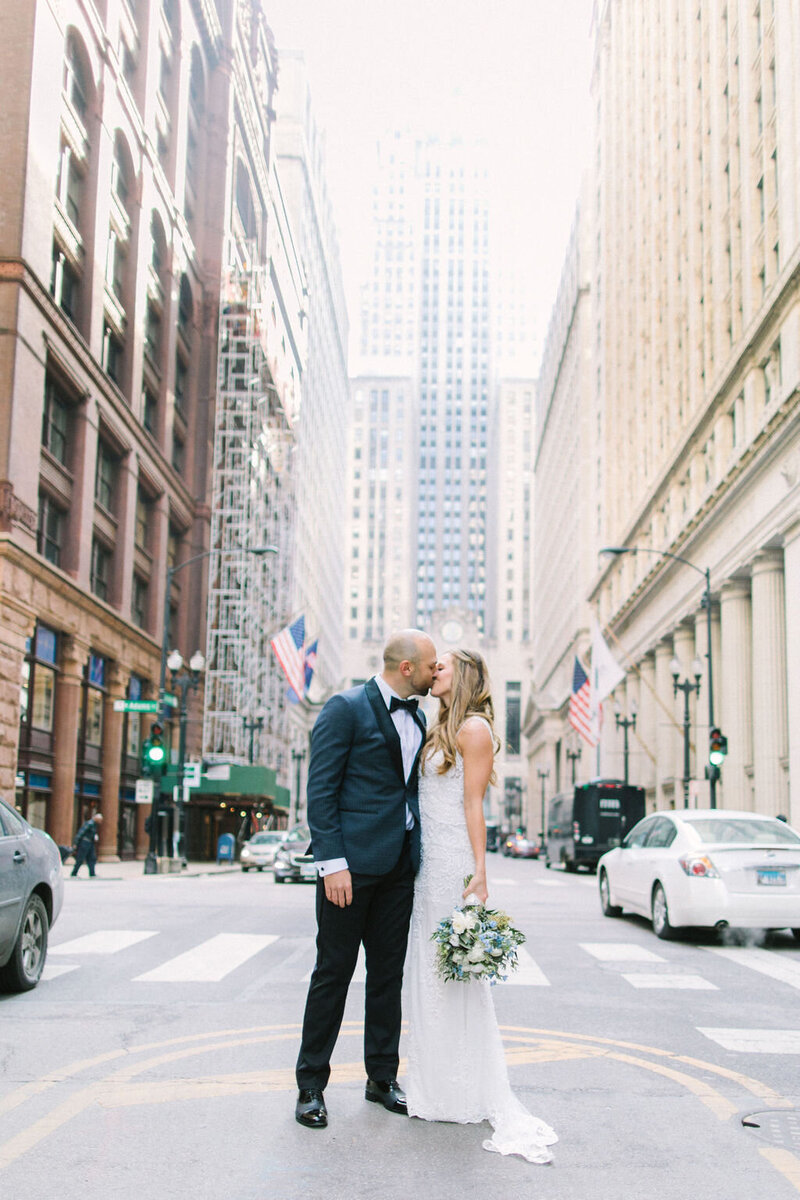 Bride and groom kissing in front of city buildings.