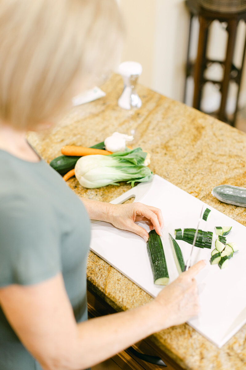 A person cutting cucumbers on a cutting board in a well-lit kitchen.