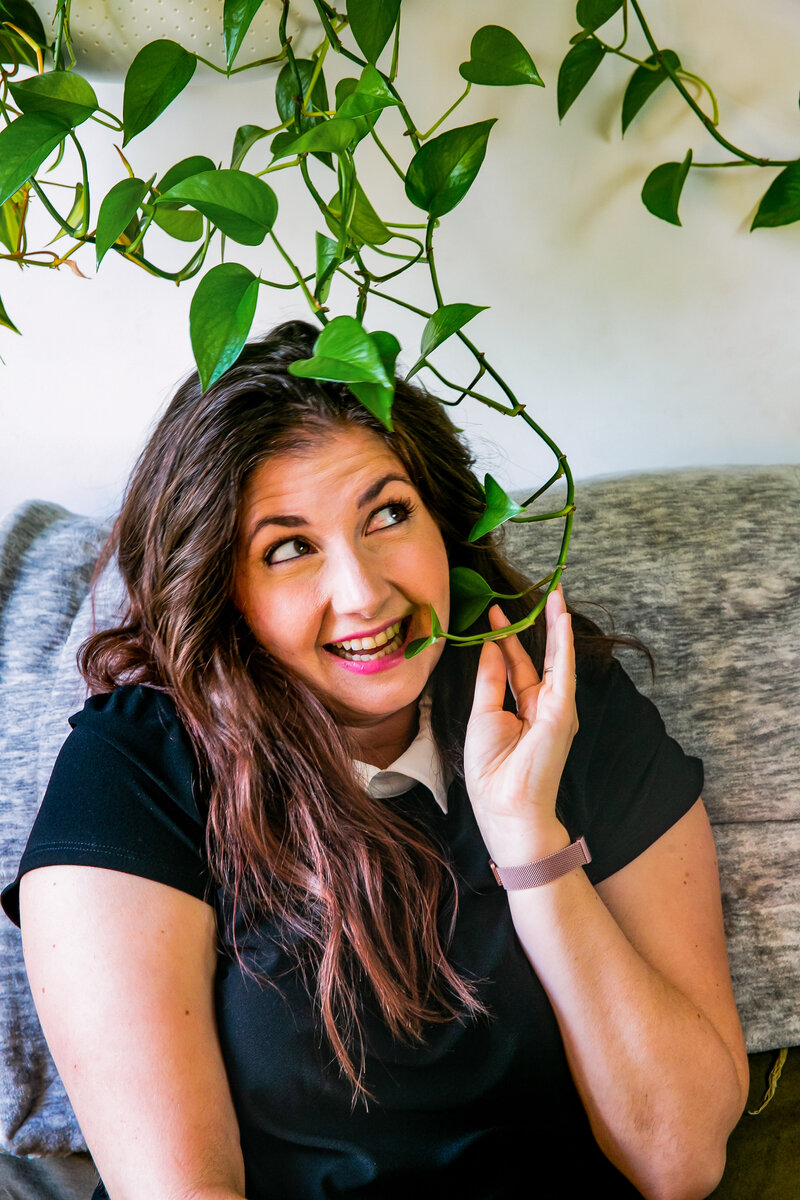 Woman smiles on her sofa while holding leaves of wall climbing plant