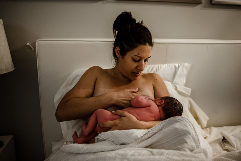 Woman lying in bed breastfeeding a newborn baby