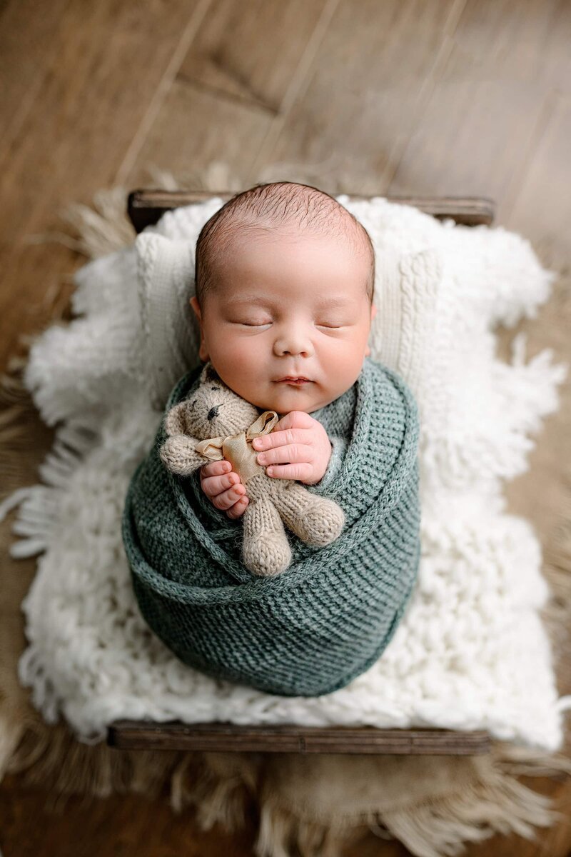 newborn baby wrapped in green snuggling a stuffy on a bed
