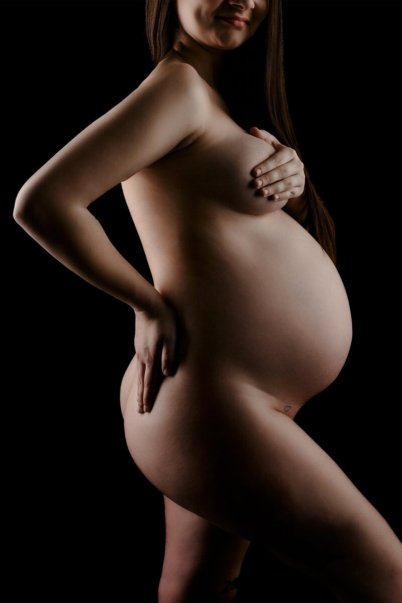 photo of uncovered pregnancy belly where the mom has on hand on her back hip and her other over her breast