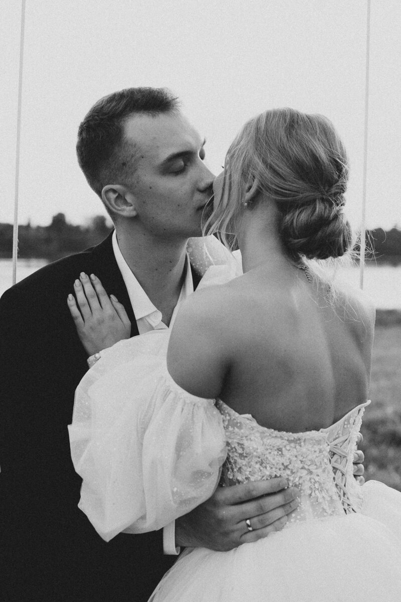 black and white image of bride and groom kissing in a field
