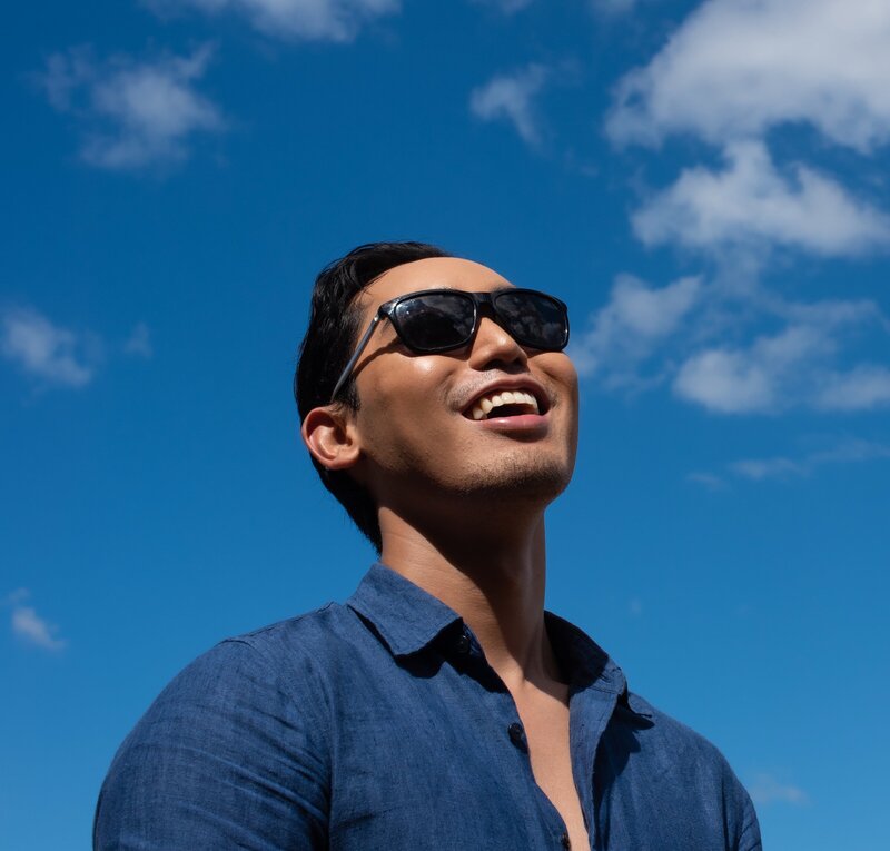 Headshot of Aleczander Gamboa with sunglasses  wearing blue linen and looking up at the sky.