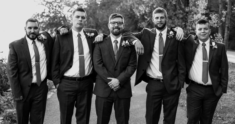 Groom stands with his groomsmen on the walking path at Presque Isle State Park