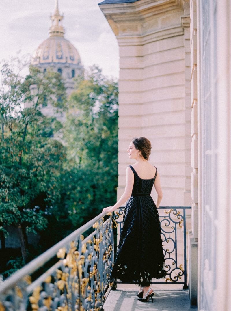 Woman in black dress standing on ornate balcony in Paris
