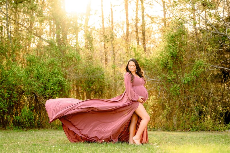 A rose pink dress Flows In The Wind as this expectant mom is posed with her chin towards her shoulder in a dramatic fashion for her maternity photography session
