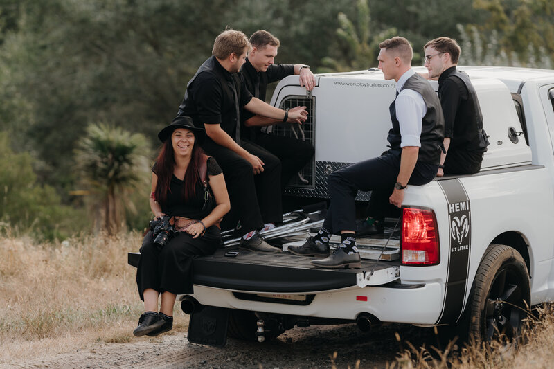 Tashina Narelle Photo + Video sitting ont he back of a four wheel drive vehicle with the groom and groomsmen during a ohotoshoot at a wedding in Auckland