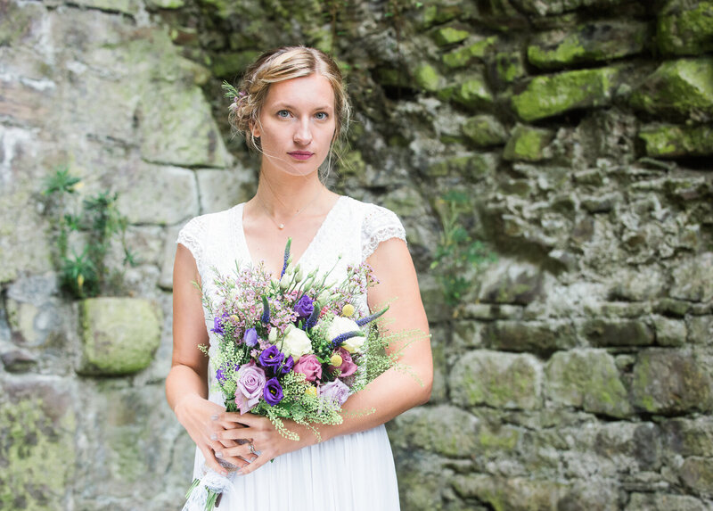 Bride with blonde hair, standing in castle in Ireland with wild flower bouquet