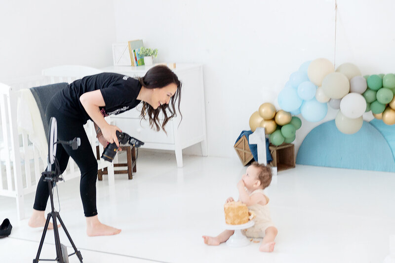 A photographer plays and laughs with a toddler smashing a cake