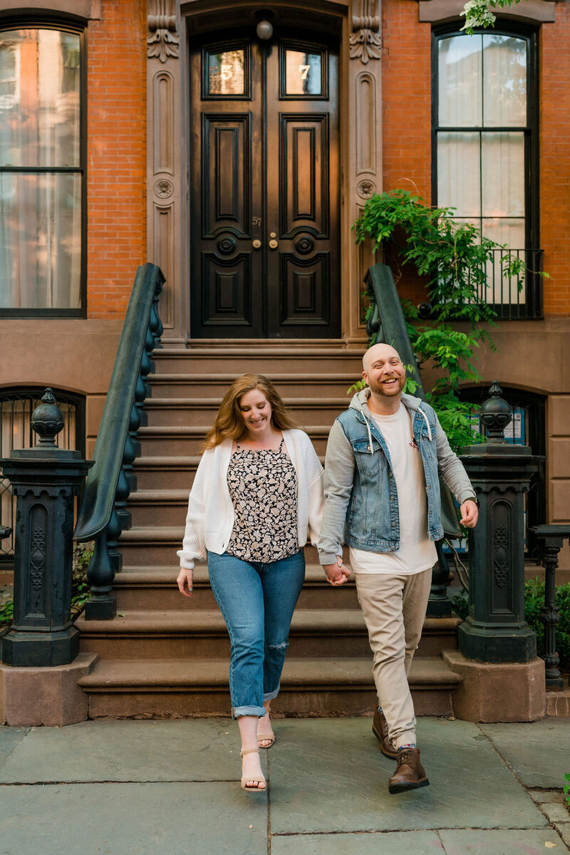 couple holding hands and looking at each other as they walk down a sidewalk laughing