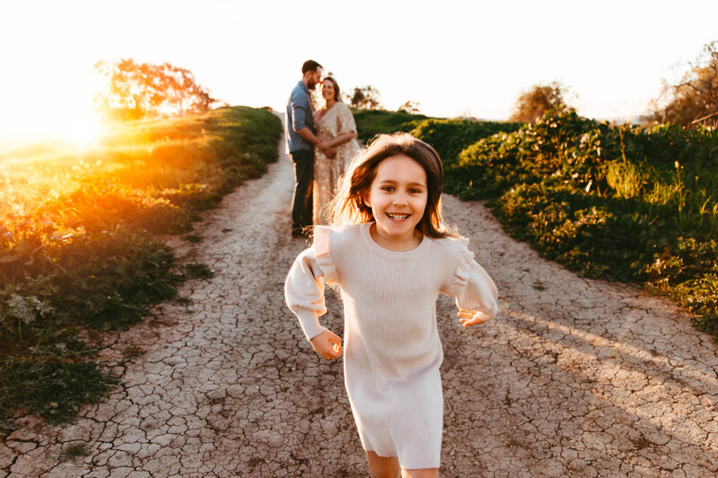girl running at camera with parents in background
