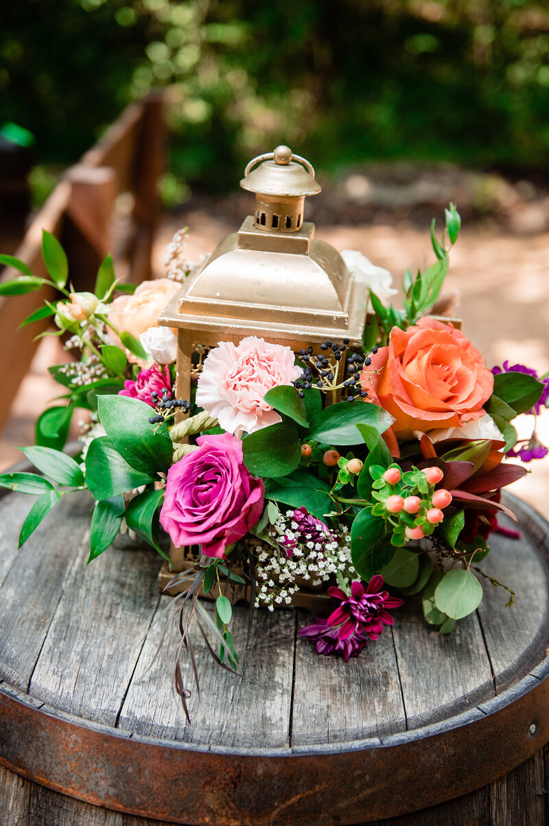 Bright pinks and orange flowers on a barrel at ceremony aisle