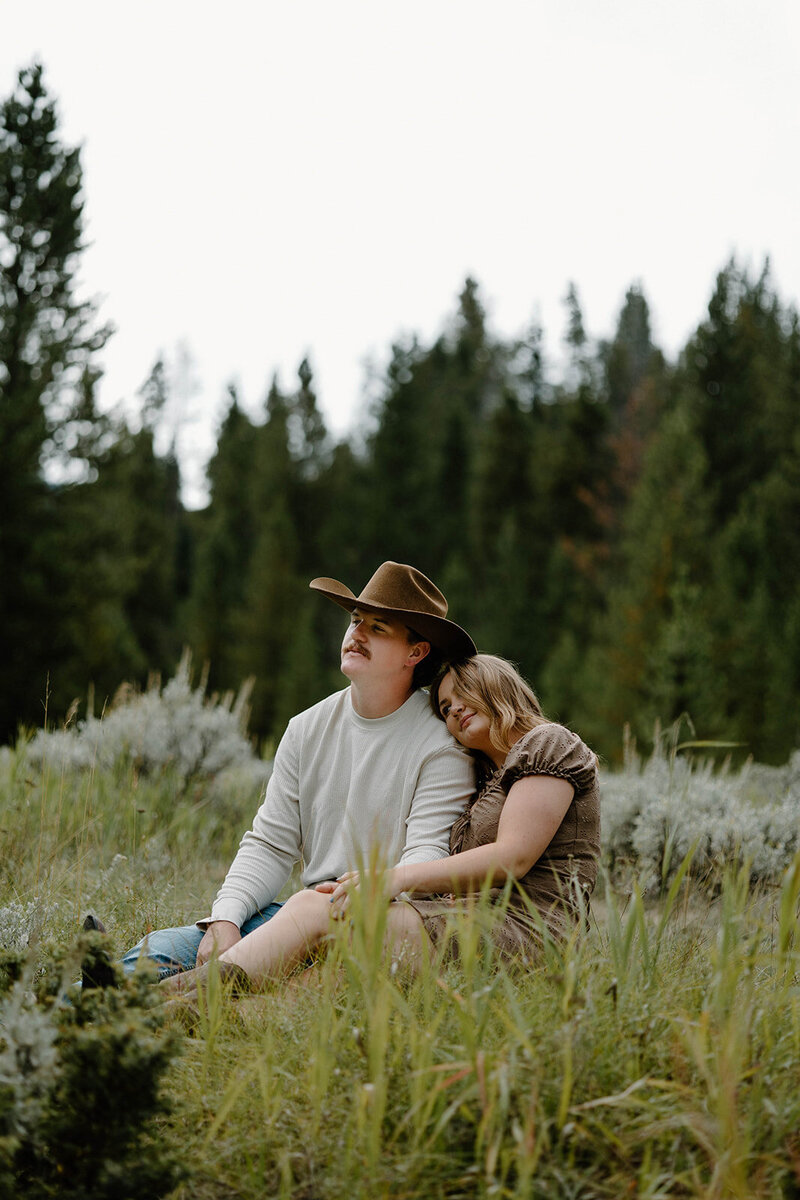 Woman lays her head on her fiancee's shoulder in adventurous West Yellowstone engagement photoshoot in Montana.