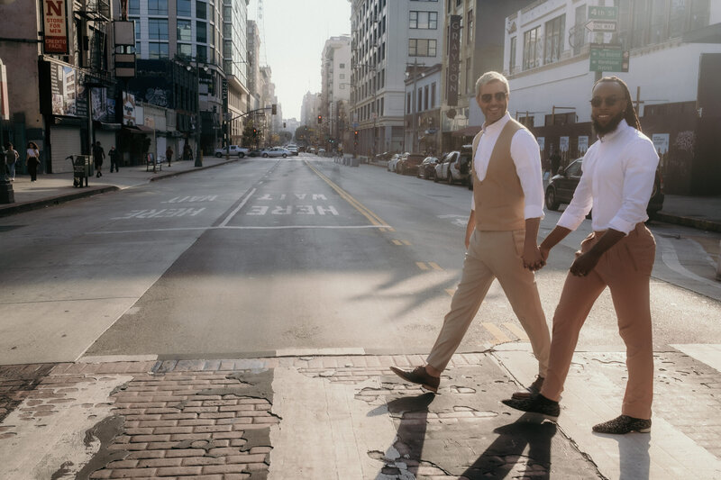 Das glückliche LGBTQIA+-Paar überquert bei einem Fotoshooting im Freien in Los Angeles eine Straße.