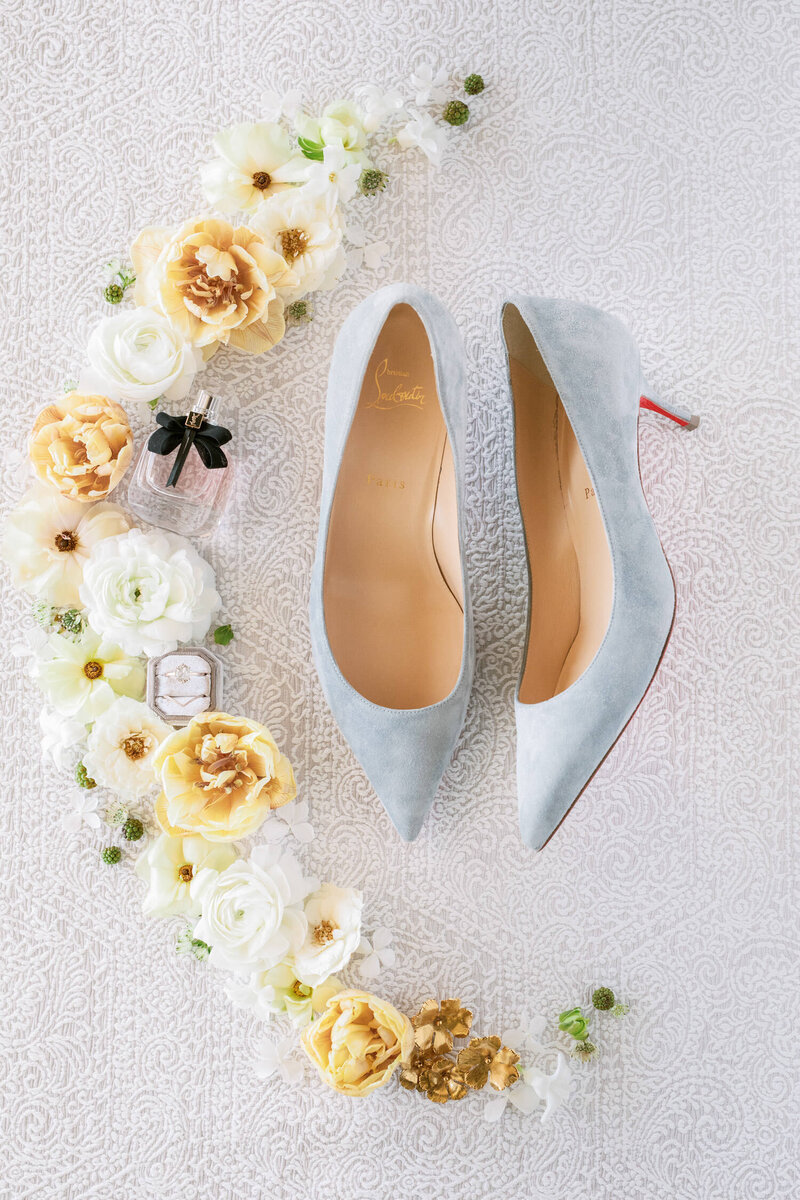 Stunning flat lay image of light blue Christian Louboutin wedding heels, flowers, and wedding rings