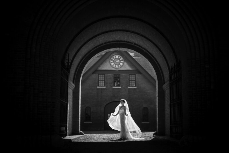 A bride standing under a large outdoor archway.