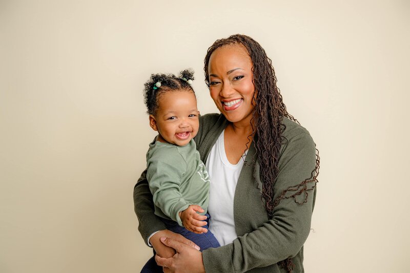 mom and daughter are dressed in green as mom holds her on her hip