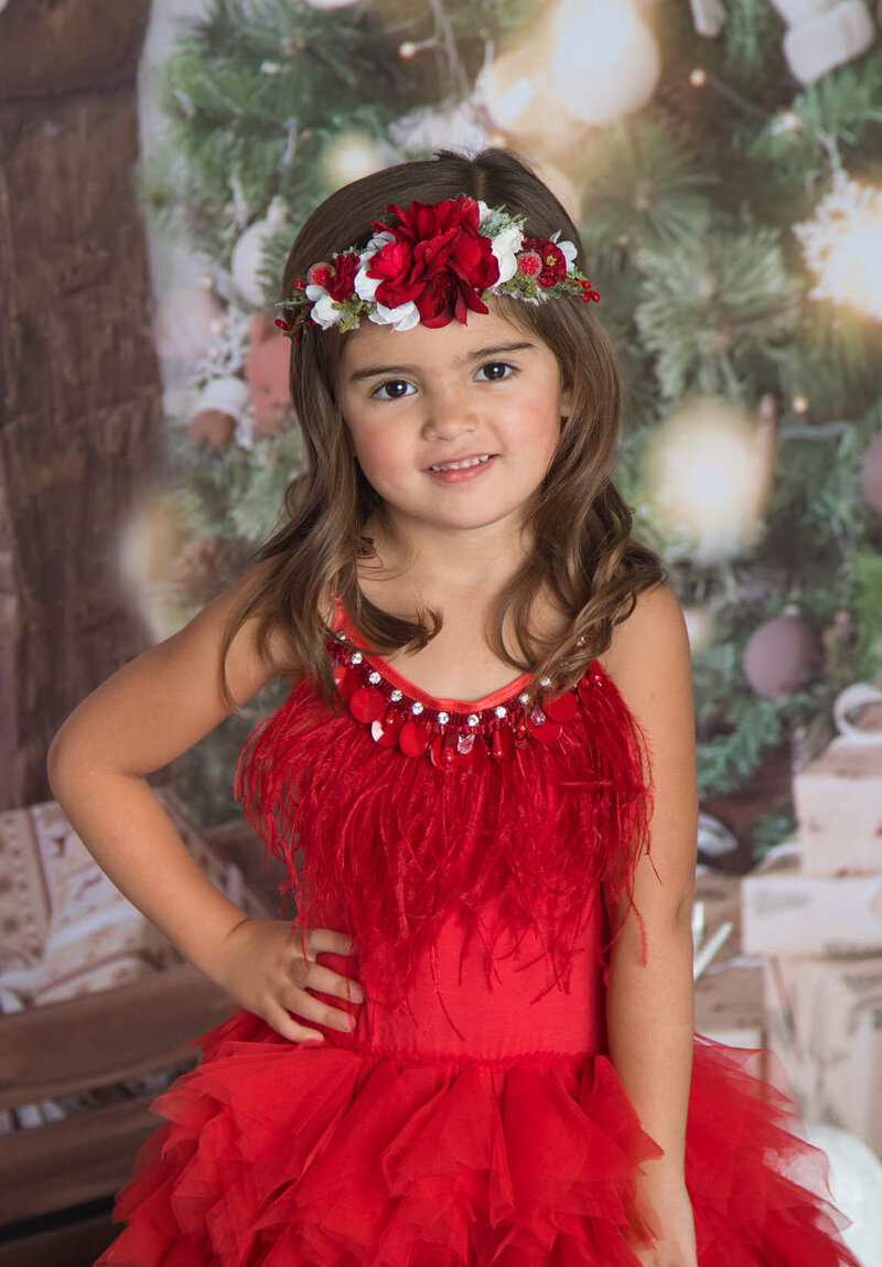girl-in-red-ttdm-dress-with-hand-on-hip-in-studio-arlington-tx-with-holiday-backdrop