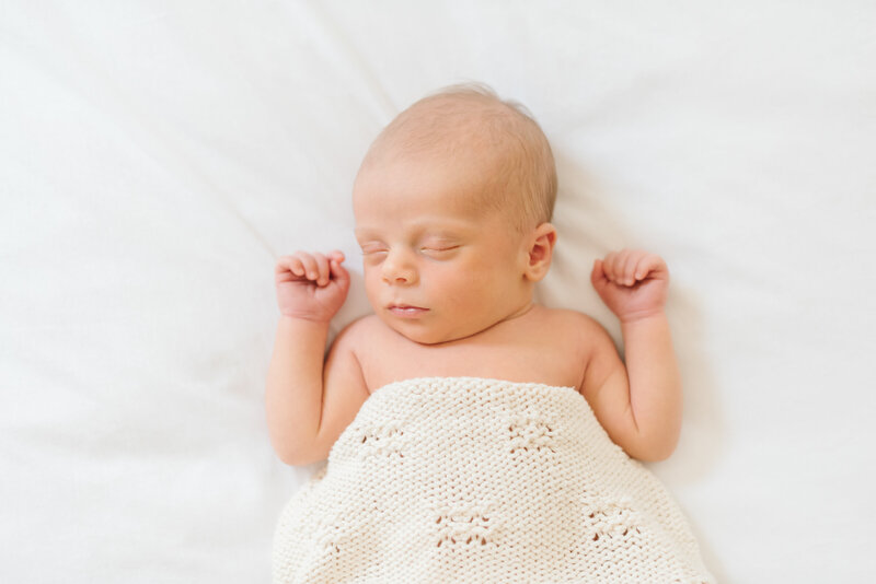 Newborn baby asleep on a white blanket covered in white quilt - Northern Virginia Newborn Photographer