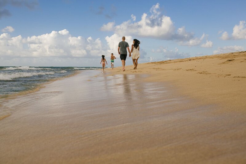 A mother and father hold hands along their beach, why their two children run ahead along the sand.