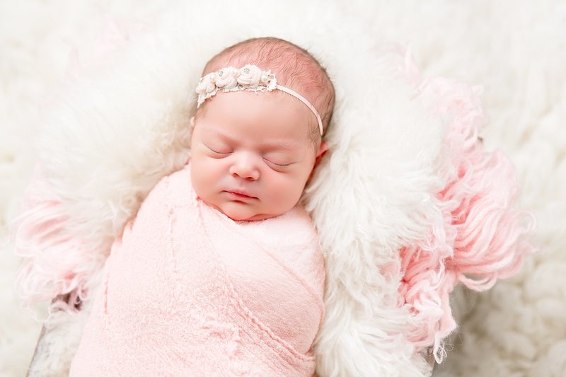 newborn wrapped in pink with white flower headband