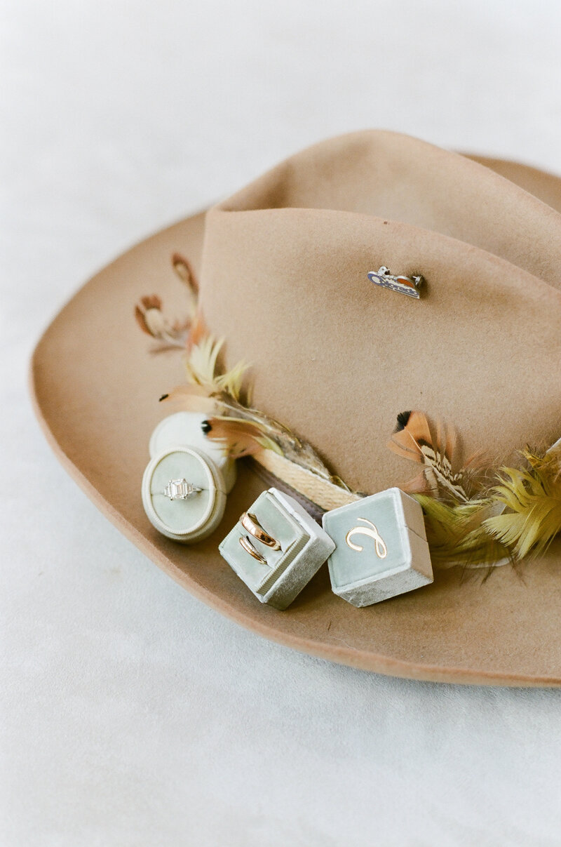 Wedding accessory details, a feather trimmed tan cowboy hat and wedding rings in decorative blue boxes