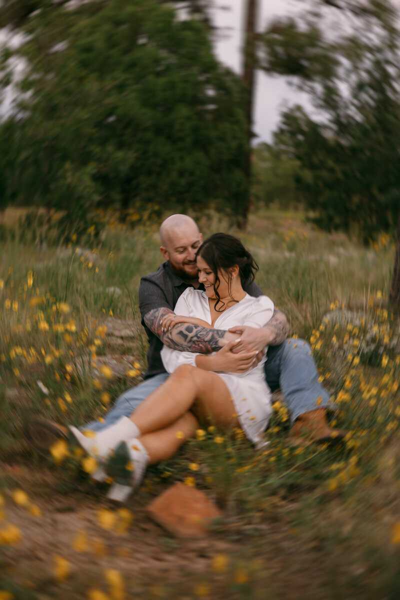 A couple sitting with their arms around each other in a field.