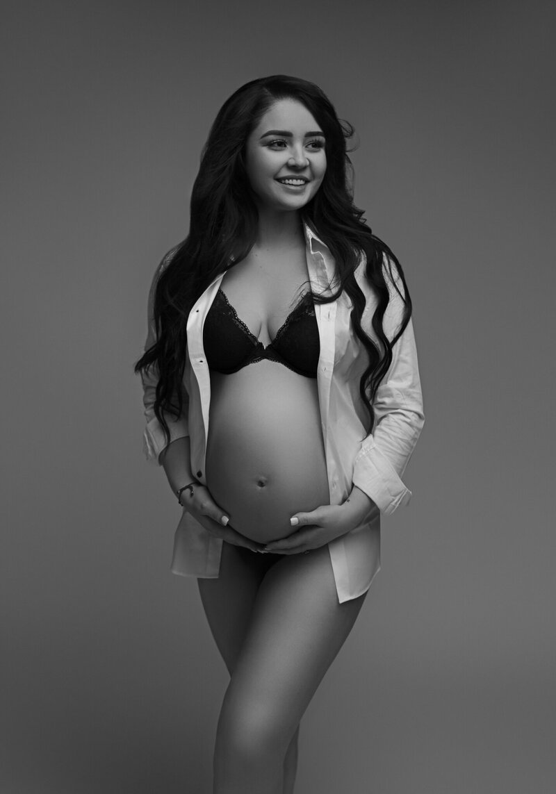 Studio maternity portrait of woman in long-sleeved white dress shirt cradling baby bump at Tamara Hudson Studios in Tacoma