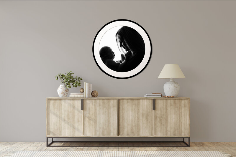 Round black framed photograph hanging in a dining room  of a  silhouette of a mother lovingly looking at her newborn baby.