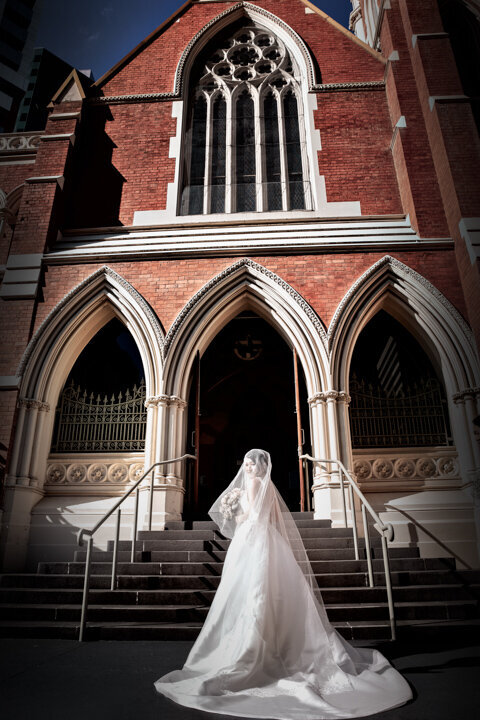 Bride is standing in front of the church with her long gown at the stairs