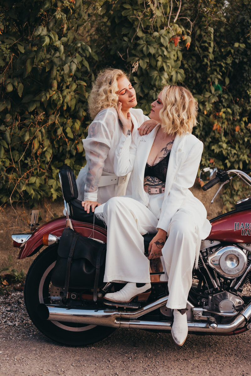 Engagement portrait of women sitting on motorcycle looking at each other