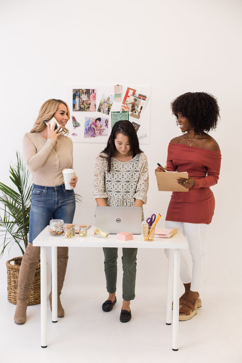 3 adult women standing over desk talking