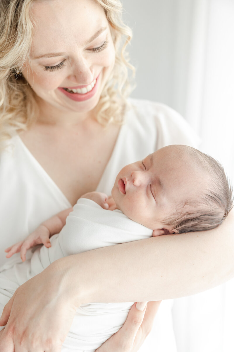 New mom smiles as she looks down at her sleeping newborn baby during in-studio newborn photography session