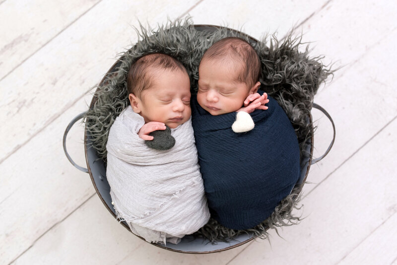 Twin boys swaddled and posed together in tub during their newborn photo session.