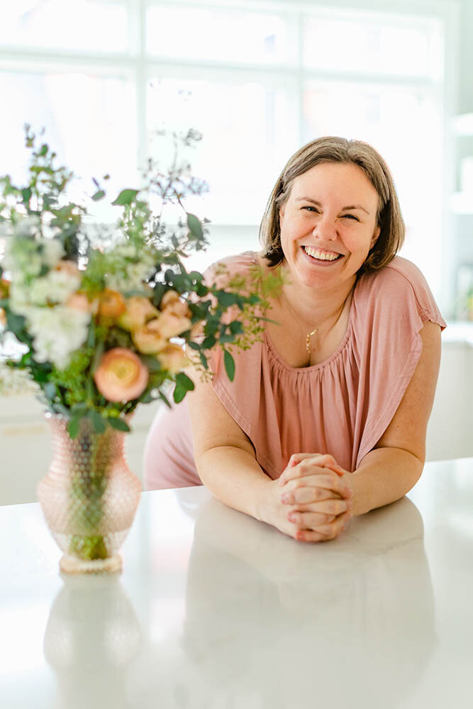 Photographer Kristen Hazelton wearing a pink dress next to a vase of flowers