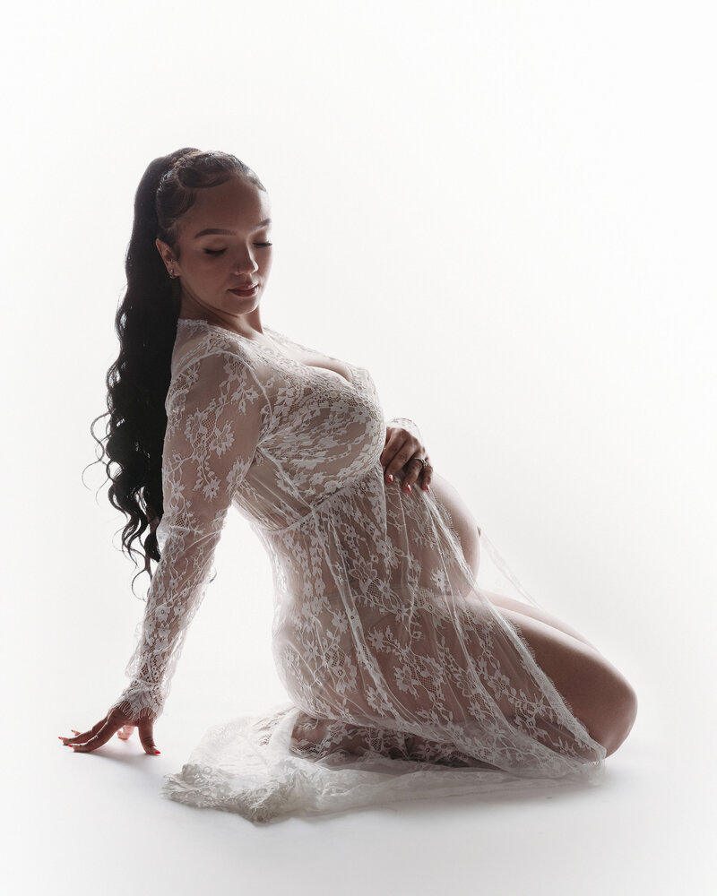 pregnant woman with long ponytail wearing lace dress with open belly holding posing
