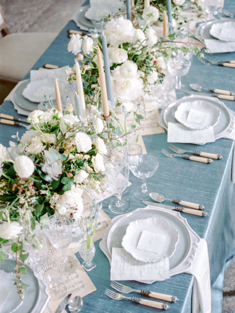 A tablescape with a blue tablecloth and white flower centerpieces