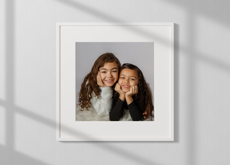 Beautiful photo of two sisters taken in studio on a grey background and ung in a white frame near a window