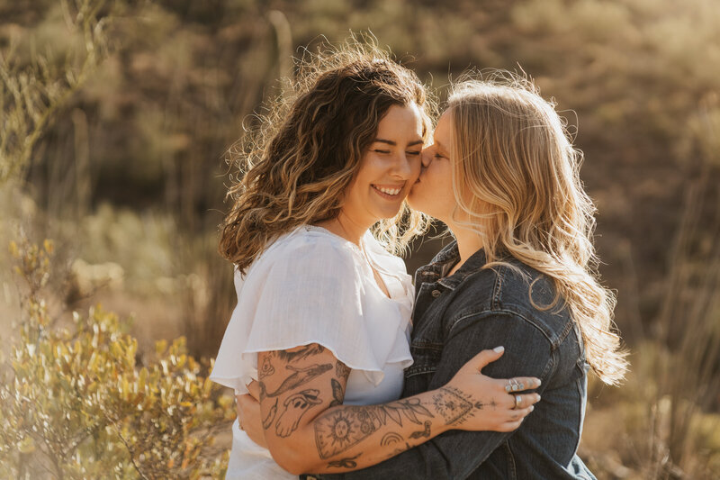 A person kissing their partner on the cheek as they have their arms around each other 