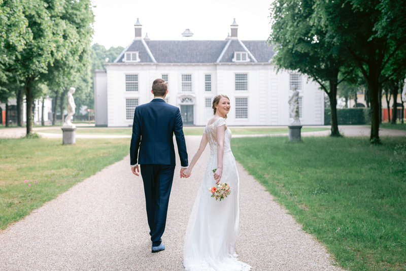 Bruidspaar wandelt terwijl de bruid achterom kijkt op landgoed Beeckestijn in Velsen