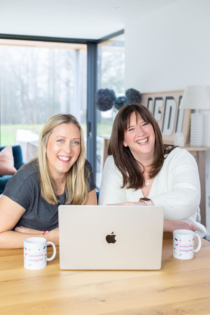 the two lauras leaning on a worktop smiling. They both have a mug in front  of them with the two lauras logo on