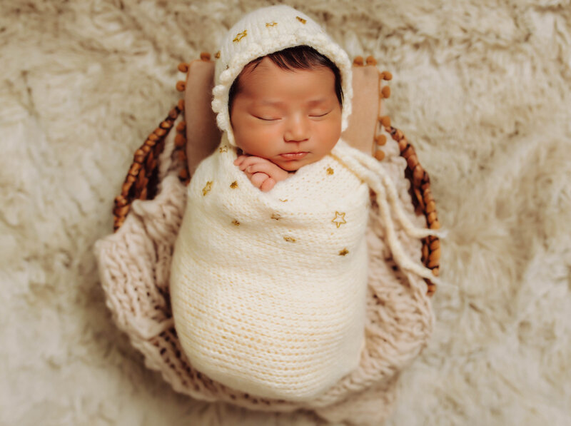 Newborn baby wrapped in white laying on a basket
